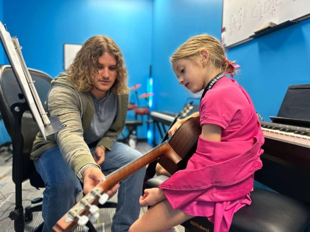 A young student learning acoustic guitar with her BLE teacher
