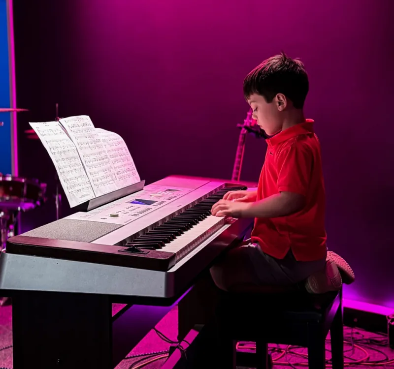 A BLE student playing piano on stage under pink lights