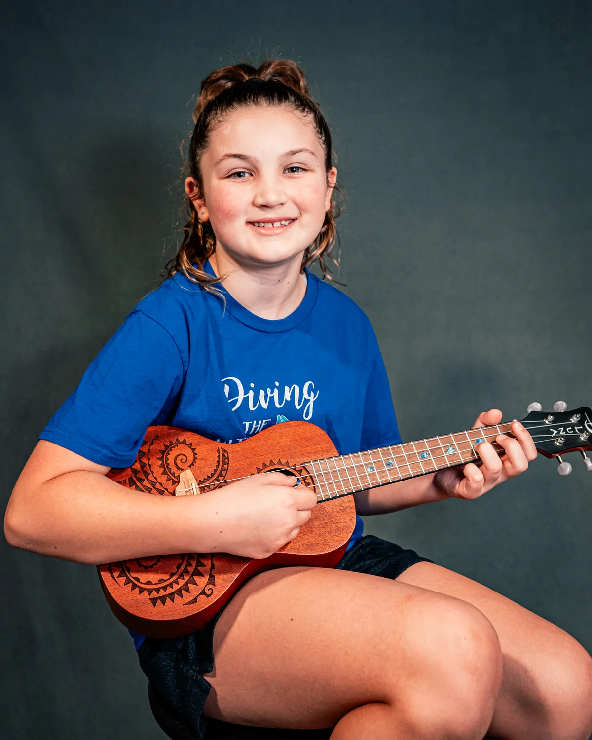 A young BLE musician fretting and strumming a four-string ukulele